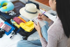 Asian Girl Packing Suitcase and Marking Off Checklist